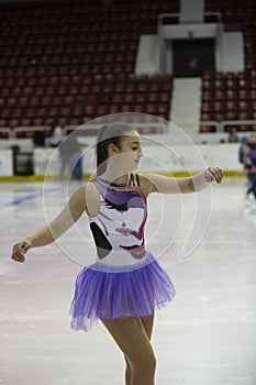 Young girl a figure skater in purple dress on an ice arena