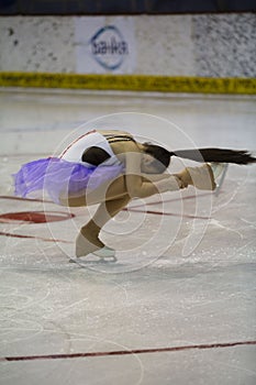 Young girl a figure skater in purple dress on an ice arena