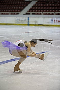 Young girl a figure skater in purple dress on an ice arena