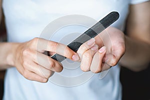 A young girl files her nails with a black nail file close-up. Women`s nails and nail file. Self-manicure at home for yourself. A w