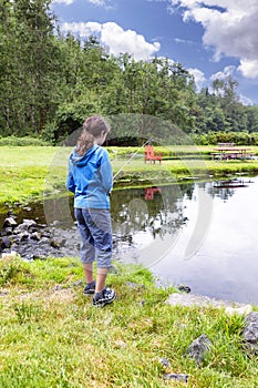 Young girl fishing on pond during bright summer day