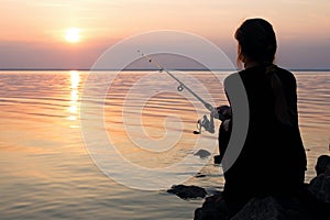 Young girl fishing at sunset near the sea