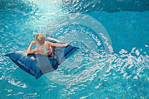Young girl on floating bean bag relaxing in swimming pool