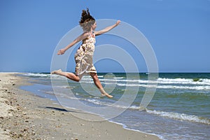 Young girl in a floral dress froze in a jump on the background of the sea and blue sky