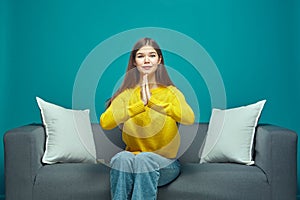 Young girl folded hands asking help or forgiveness, pleading, worried about series or movie end, sitting on sofa