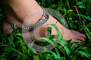 A young girl foot wearing anklet or payel and stepping on the green grasses. Young woman foot with silver ankle