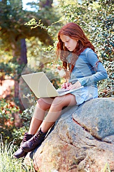 Young girl, forest and laptop on rock for internet, break and connection on holiday in woods for travel tips. Child, red