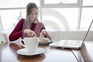 Young girl freelancer sits in a cafe with a laptop, drinks coffee and has breakfast, a student eats in the morning with a computer
