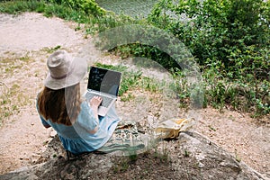 A young girl freelancer works with a laptop in nature
