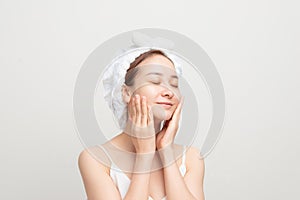 Young girl with fresh and clean skin, wearing white bath towel on her head, touching her face, looking with cute smile against