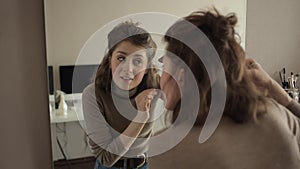 A young girl in front of a mirror examines her hair and pulls out gray hair