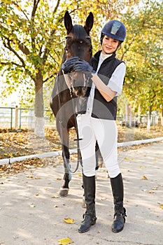 A young girl in full growth in an autumn park hugged the horse`s face with her hands.