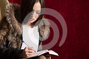 Young girl in a fur coat sits back and takes notes