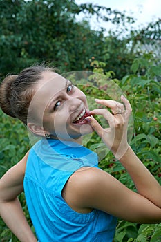 Young girl in garden with raspberries in your mouth smiles