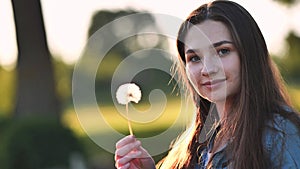 A young girl gently looks at the dandelion flower.