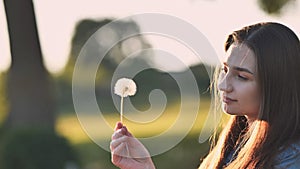 A young girl gently looks at the dandelion flower.