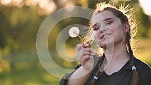 A young girl gently looks at the dandelion flower.