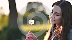 A young girl gently looks at the dandelion flower.