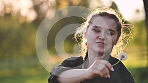 A young girl gently looks at the dandelion flower and blows it away.