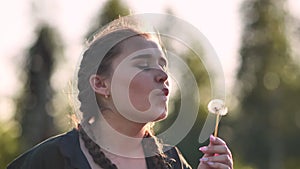 A young girl gently looks at the dandelion flower and blows it away.