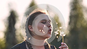 A young girl gently looks at the dandelion flower and blows it away.