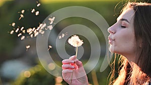 A young girl gently looks at the dandelion flower and blows it away.