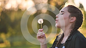 A young girl gently looks at the dandelion flower and blows it away.