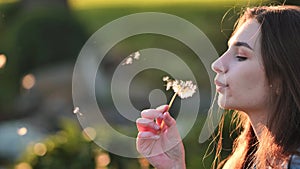 A young girl gently looks at the dandelion flower and blows it away.