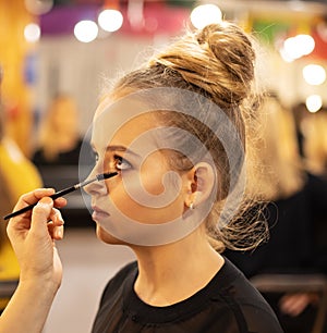 Young girl getting eye makeup. Make-up artist using brush - closeup