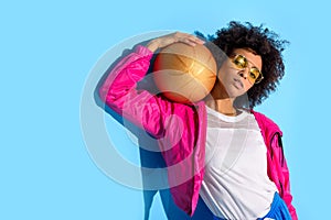 Young girl in glasses holding basketball ball and looking at camera on blue