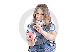 Young girl in glasses puts a coin into a piggybank