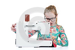 Young girl with glasses sews on a sewing machine, isolated on white background