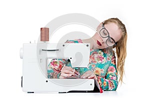 Young girl with glasses sews on a sewing machine, isolated on white background
