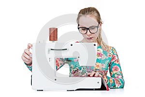 Young girl with glasses sews on a sewing machine, isolated on white background