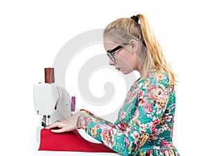 Young girl with glasses sews on a sewing machine, isolated on white background