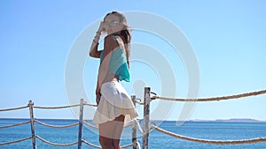 young girl in glasses stands near the sea keeps your hand near the face and poses for the camera in slow motion