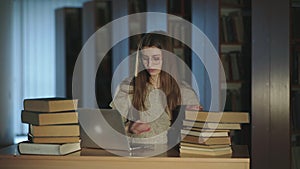 Young girl in glasses working hard with laptop and books at desk in library