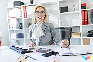 Young girl with glasses works in the office with documents, calculator and computer.