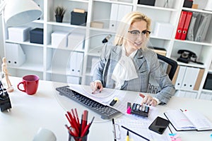 Young girl with glasses works in the office with documents, calculator and computer.