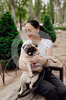 Young girl goes for walk with doggy pug in park. Selective focus