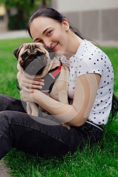 Young girl goes for walk with doggy pug in park. Selective focus