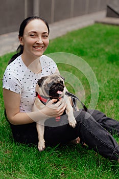Young girl goes for walk with doggy pug in park. Selective focus