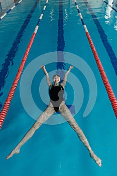 Young girl in goggles and cap swimming on the back of in the blue water pool. Sporty woman relax in the blue water.