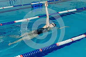 Young girl in goggles and cap swimming back crawl stroke style in the blue water pool