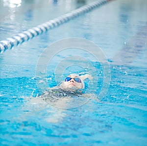 Young girl in goggles swimming back crawl stroke style