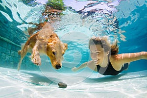 Young girl with golden retriever dog diving in swimming pool