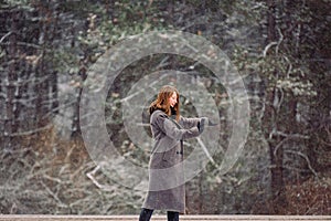 A young girl in a gray coat is keen on photography. Taking pictures of the winter forest and beautiful scenery on the
