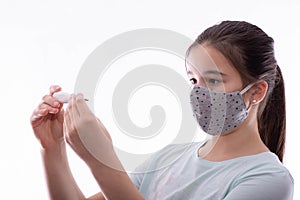 Young girl with a gray mask on her face looks at a thermometer