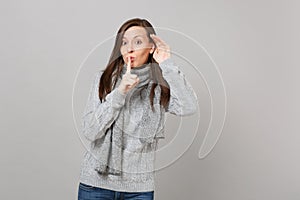 Young girl in gray sweater scarf saying hush be quiet with finger on lips shhh gesture eavesdrop and hearing on