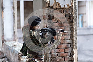 A young girl with a green camouflage uniform and a black beret with a gun among the ruins. Girl warrior with weapons